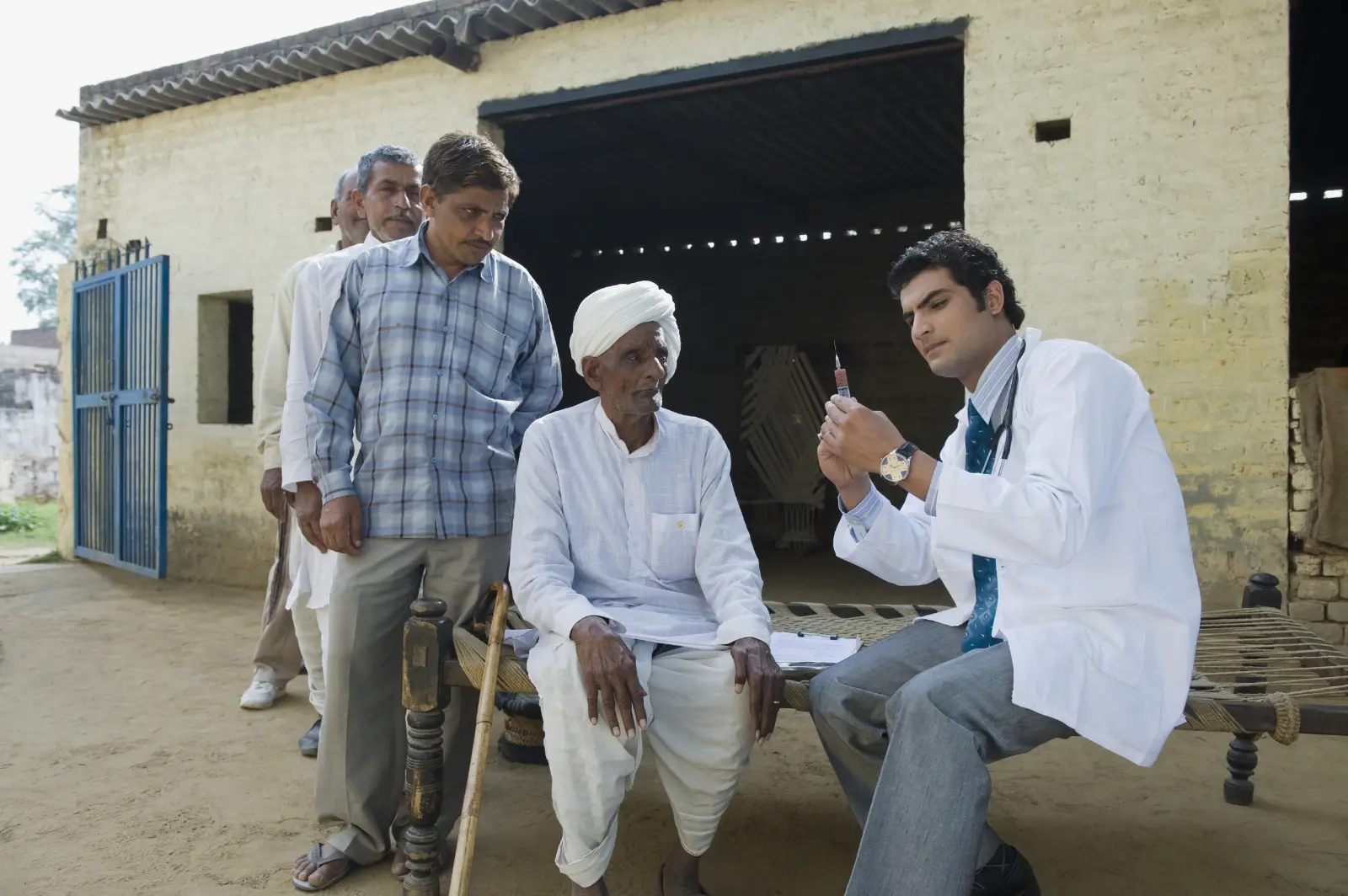 Epidemics That Didn't Happen: A doctor sitting outside in a courtyard preparing a vaccine syringe for a patent, while three others wait in a queue behind him.