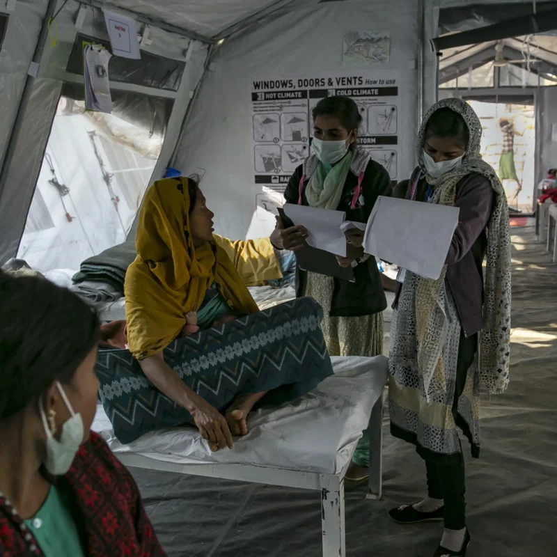 A woman being attended to by two masked nurses in a hospital tent