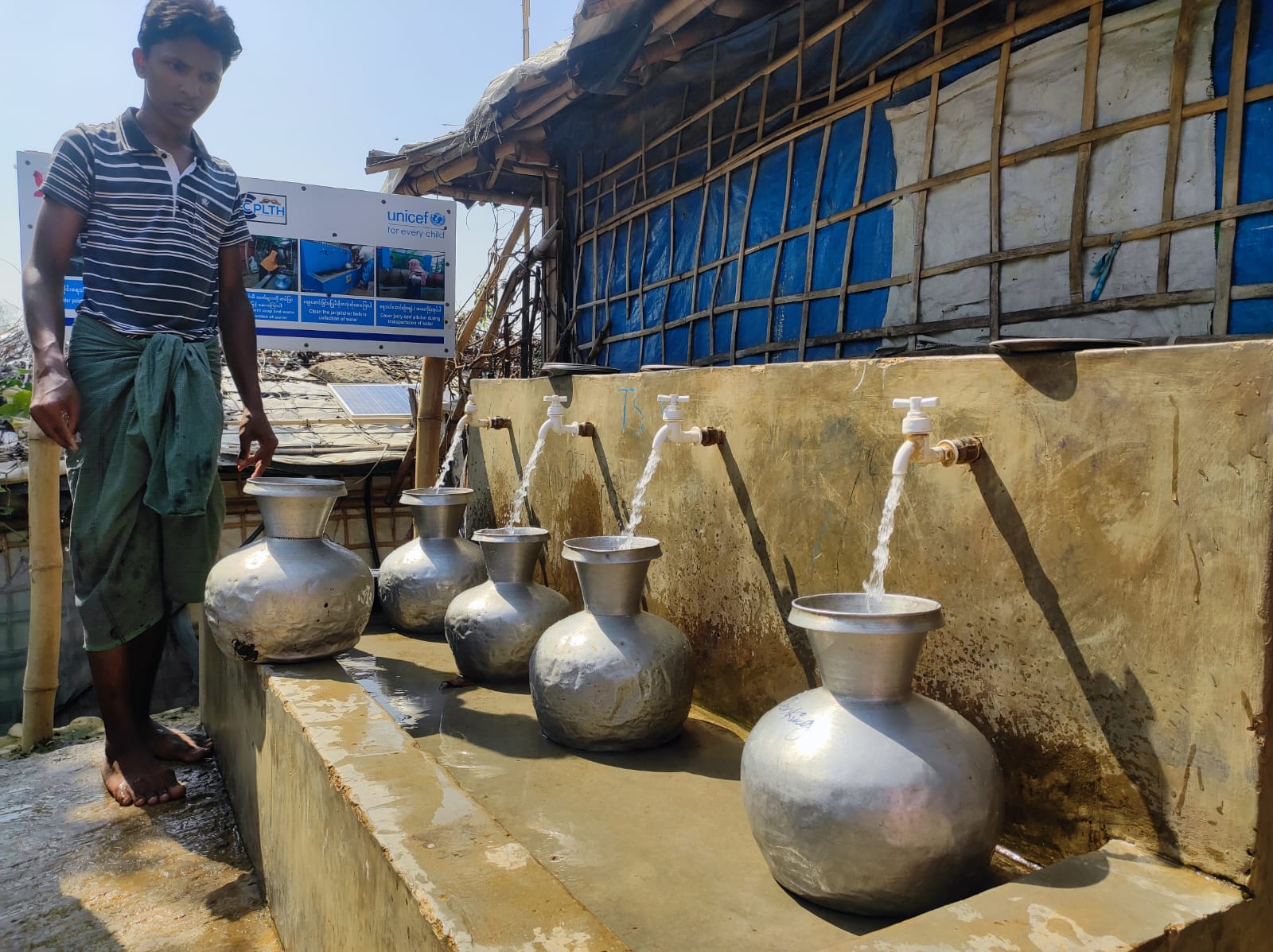 A man watches as four taps of clean water flow into metal jugs