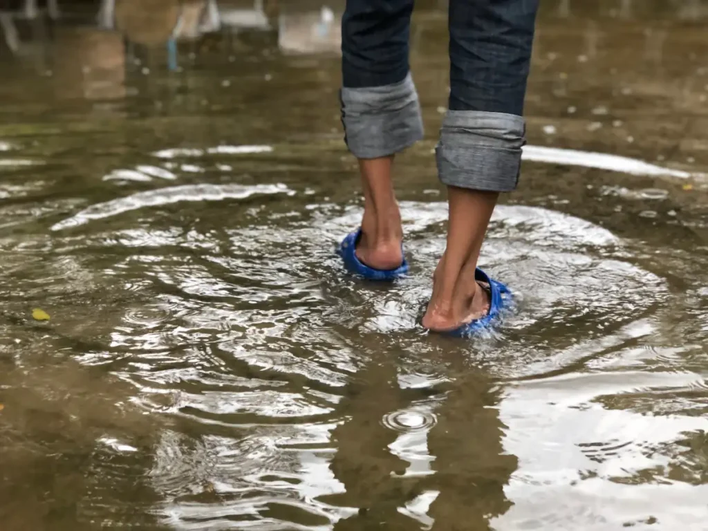 Feet walking through flood water in sandals, with jeans rolled up to keep them dry